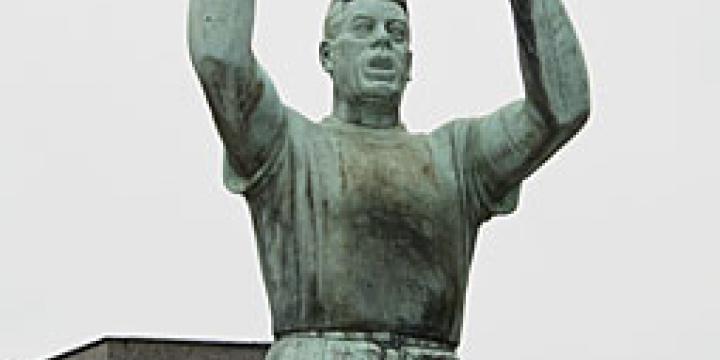 Le monument Julien Lahaut au cimetière de Seraing. Inauguré sous sa forme définitive en 1956, il comporte une statue de l'homme politique dans sa posture familière de tribun et, derrière lui, un monument plus massif symbolisant le 'peuple', que Lahaut paraît protéger. (Photo équipe projet Lahaut, Cegesoma)