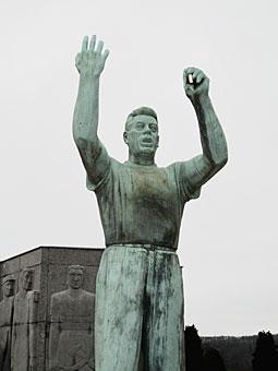 Le monument Julien Lahaut au cimetière de Seraing. Inauguré sous sa forme définitive en 1956, il comporte une statue de l'homme politique dans sa posture familière de tribun et, derrière lui, un monument plus massif symbolisant le 'peuple', que Lahaut paraît protéger. (Photo équipe projet Lahaut, Cegesoma)